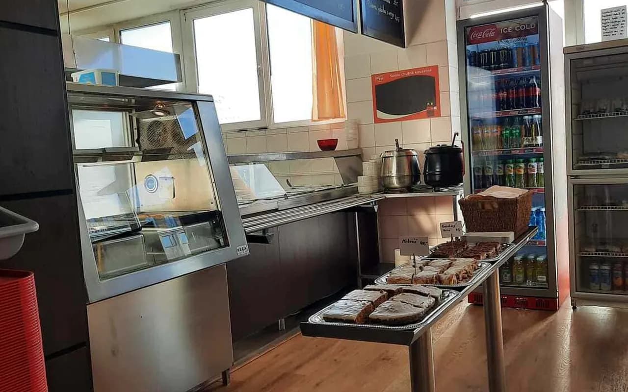 Výdejní pult jídelny s křídovými tabulemi denního menu a chlazenými nápoji
