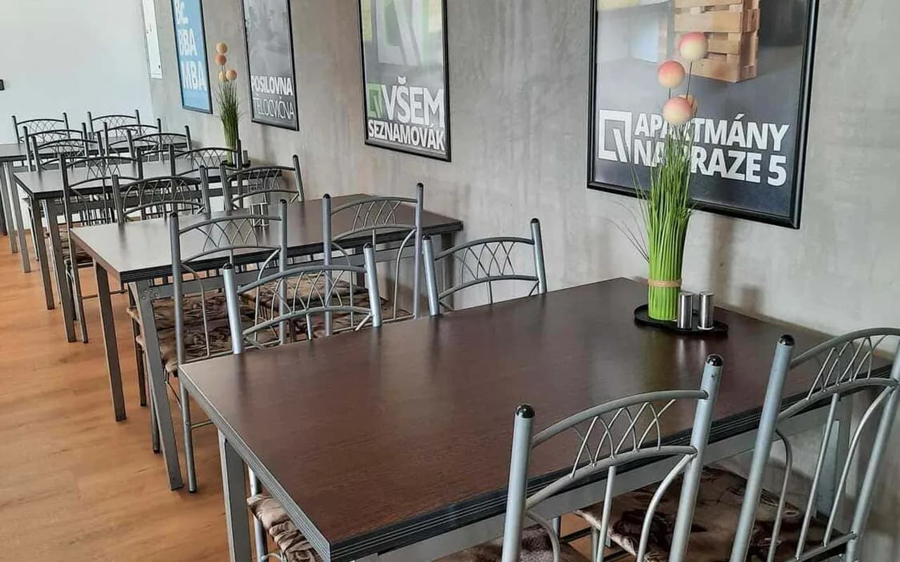 Řada stolů v jídelně s obrazy Campusu VŠEM na betonové stěně